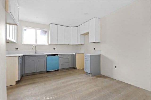 kitchen featuring dishwasher, light wood finished floors, a sink, and gray cabinetry