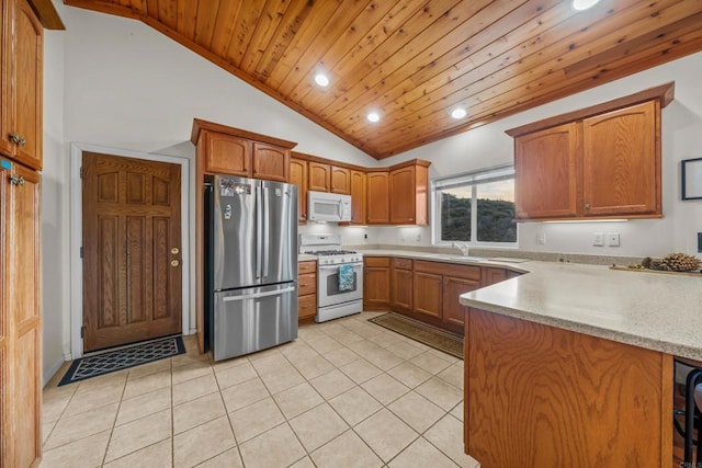 kitchen with a sink, white appliances, a peninsula, light countertops, and light tile patterned floors