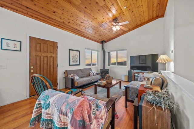 living room with light wood-type flooring, wooden ceiling, ceiling fan, a wood stove, and vaulted ceiling