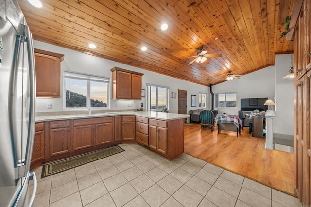 kitchen with brown cabinetry, a peninsula, stainless steel refrigerator, light countertops, and open floor plan