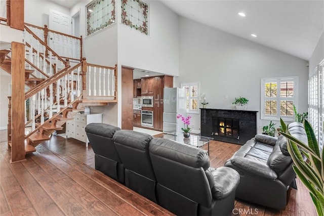 living room with high vaulted ceiling, hardwood / wood-style flooring, recessed lighting, a premium fireplace, and stairway