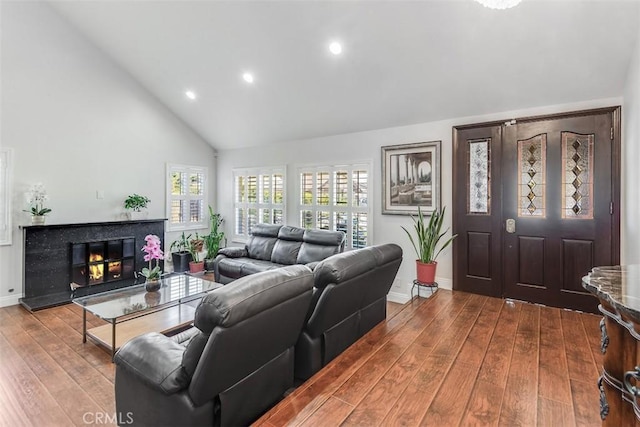 living room with high vaulted ceiling, a glass covered fireplace, wood-type flooring, and baseboards