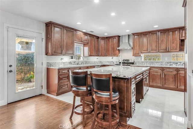 kitchen featuring a kitchen breakfast bar, stainless steel range with electric cooktop, wall chimney range hood, light stone countertops, and a center island with sink