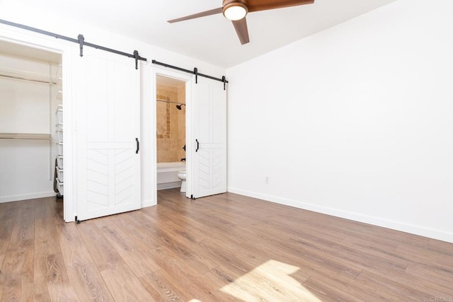 unfurnished bedroom with a barn door, baseboards, a closet, light wood-type flooring, and a walk in closet