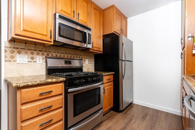 kitchen featuring stainless steel appliances, decorative backsplash, dark wood-type flooring, light stone countertops, and baseboards