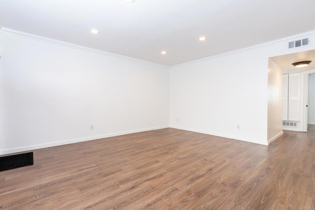 empty room with visible vents, baseboards, wood finished floors, crown molding, and recessed lighting