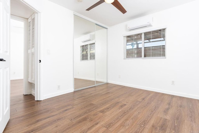 unfurnished bedroom featuring an AC wall unit, ceiling fan, baseboards, and wood finished floors