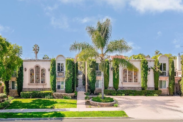 mediterranean / spanish-style home featuring concrete driveway, a front lawn, stone siding, and stucco siding