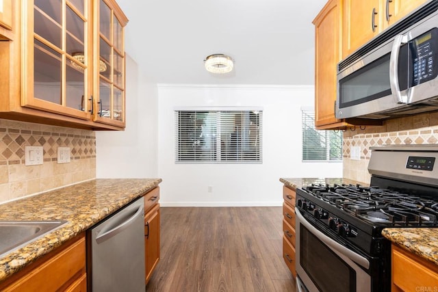 kitchen with stone countertops, dark wood-style flooring, baseboards, appliances with stainless steel finishes, and glass insert cabinets