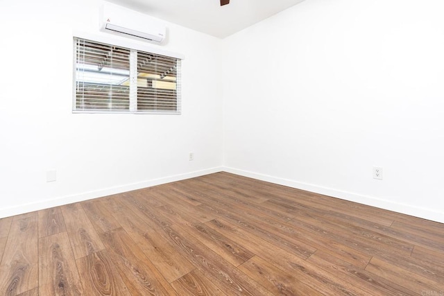 empty room with wood finished floors, baseboards, and a wall mounted AC