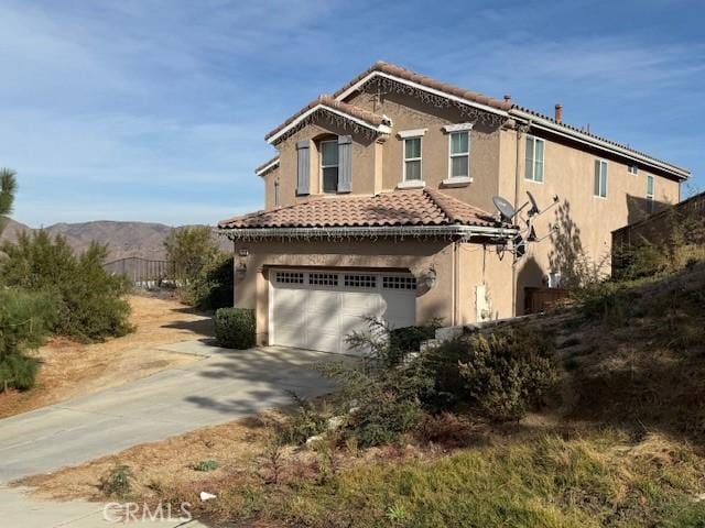 view of front of house featuring a mountain view, a garage, a tile roof, driveway, and stucco siding