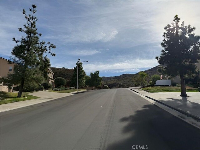 view of road featuring sidewalks, a mountain view, curbs, and street lights