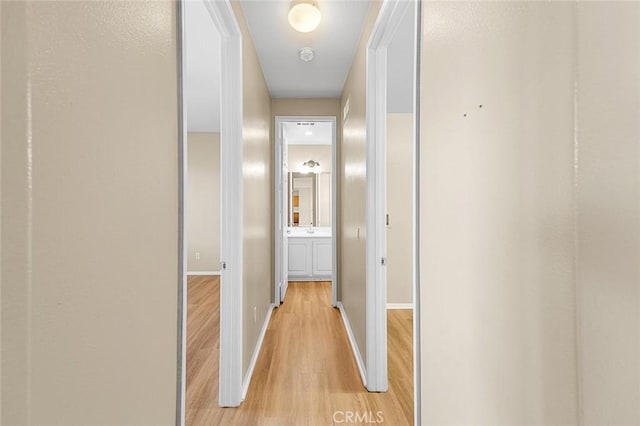 hall with a sink, light wood-style flooring, and baseboards