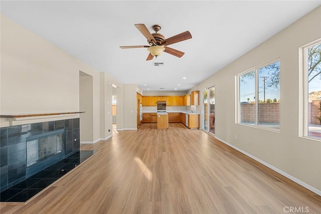 unfurnished living room featuring ceiling fan, light wood-style flooring, a fireplace, visible vents, and baseboards