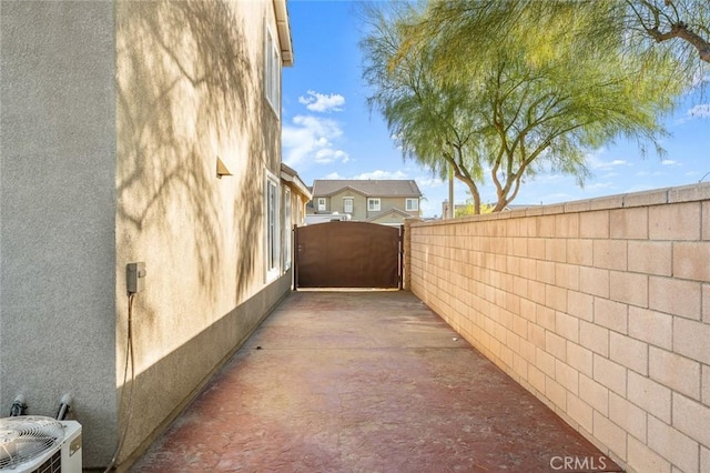 view of side of home featuring a gate, fence, central AC unit, and stucco siding