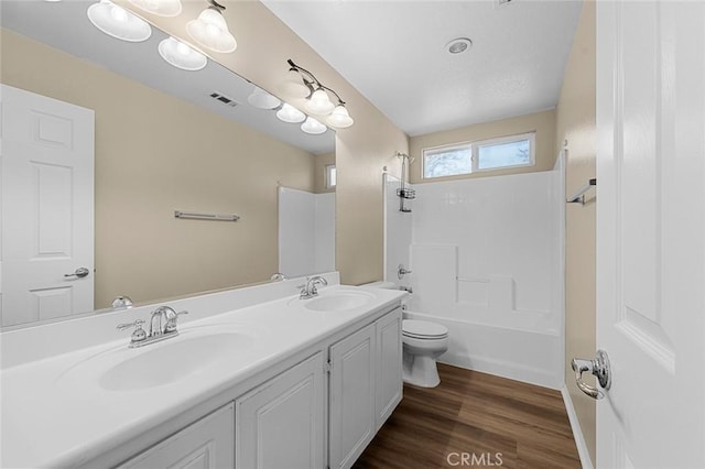 full bath with toilet, double vanity, a sink, and wood finished floors