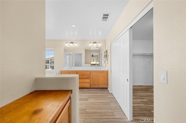 full bath with a textured wall, wood finished floors, vanity, visible vents, and a closet