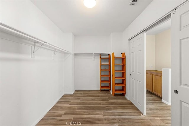 walk in closet featuring a barn door, wood finished floors, and visible vents