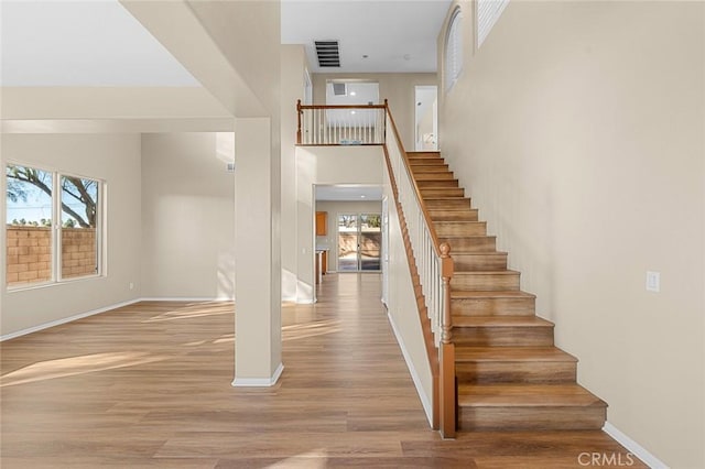 staircase with a wealth of natural light, visible vents, baseboards, and wood finished floors