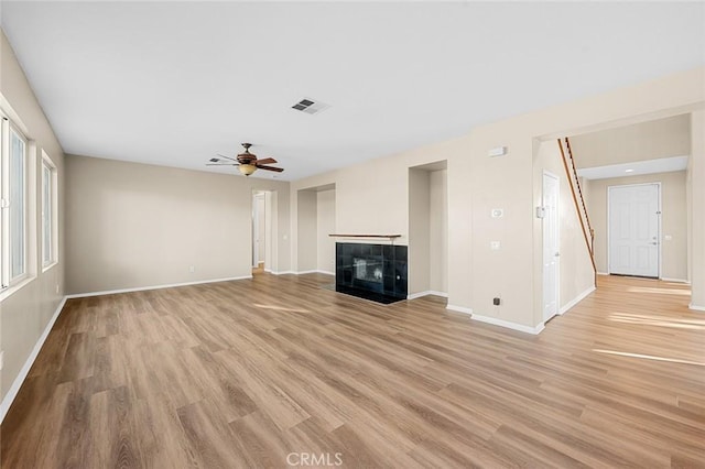 unfurnished living room with visible vents, a tiled fireplace, light wood-style floors, a ceiling fan, and baseboards