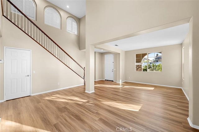 foyer with stairs, light wood-type flooring, a towering ceiling, and baseboards