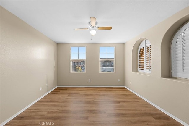 empty room with ceiling fan, wood finished floors, and baseboards