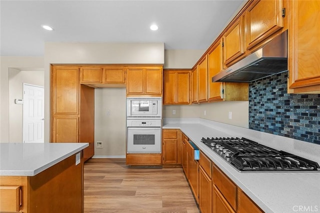 kitchen with white appliances, light wood finished floors, brown cabinetry, light countertops, and under cabinet range hood