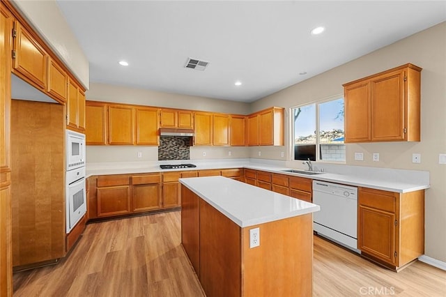 kitchen with white appliances, visible vents, light wood-style flooring, under cabinet range hood, and a sink