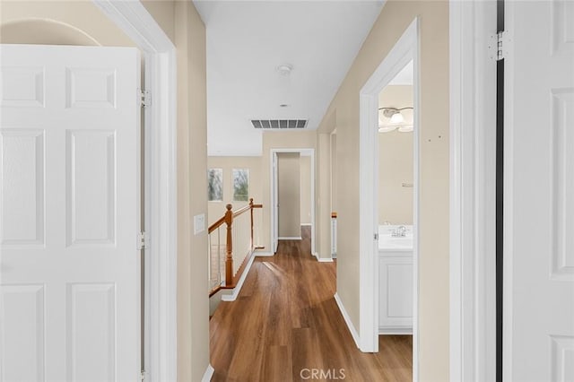 hall with visible vents, a sink, an upstairs landing, wood finished floors, and baseboards