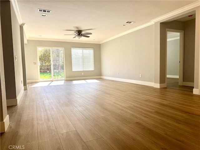 empty room featuring baseboards, crown molding, visible vents, and wood finished floors