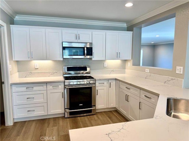 kitchen with ornamental molding, appliances with stainless steel finishes, and white cabinets