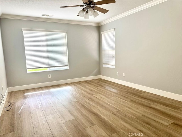 empty room featuring light wood-type flooring, visible vents, crown molding, and baseboards