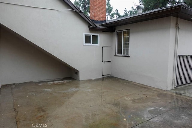 view of side of home featuring a patio area, a chimney, and stucco siding