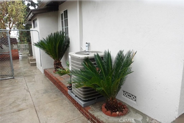 exterior space with cooling unit, a gate, a patio, and stucco siding