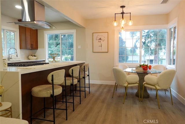 interior space with brown cabinets, light countertops, light wood-style flooring, a sink, and wall chimney range hood