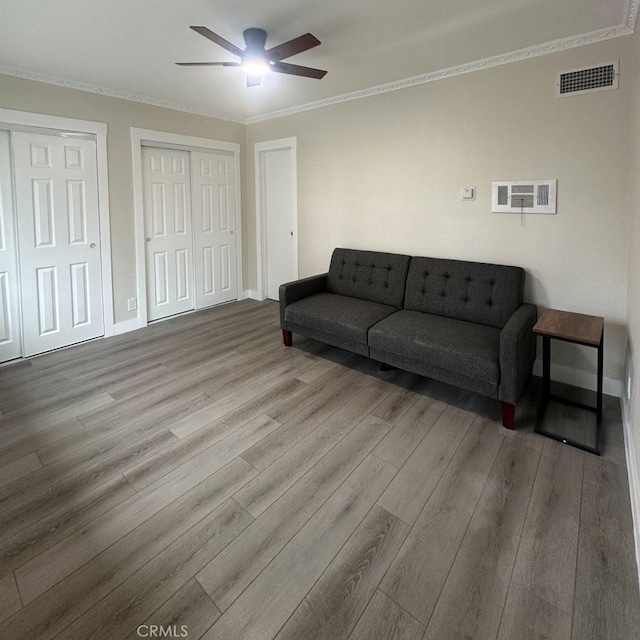 living room with crown molding, visible vents, ceiling fan, and wood finished floors