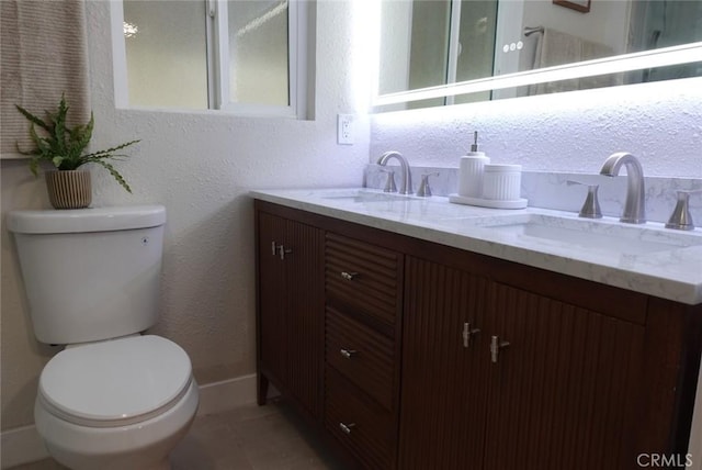 full bathroom featuring toilet, double vanity, a sink, and a textured wall