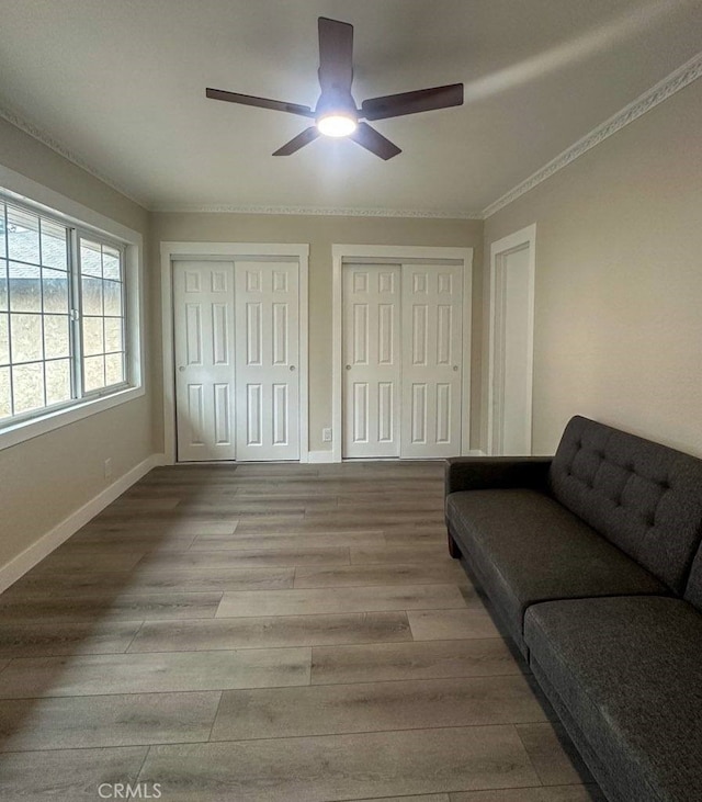 interior space with ornamental molding, wood finished floors, a ceiling fan, and baseboards