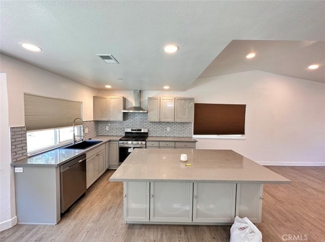 kitchen featuring visible vents, wall chimney exhaust hood, a kitchen island, stainless steel appliances, and a sink