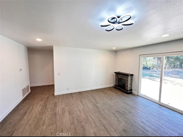 unfurnished living room with baseboards, visible vents, wood finished floors, a textured ceiling, and a fireplace