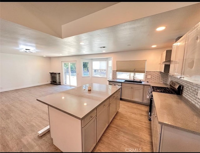 kitchen with stainless steel gas stove, decorative backsplash, a kitchen island, light wood-style floors, and a sink