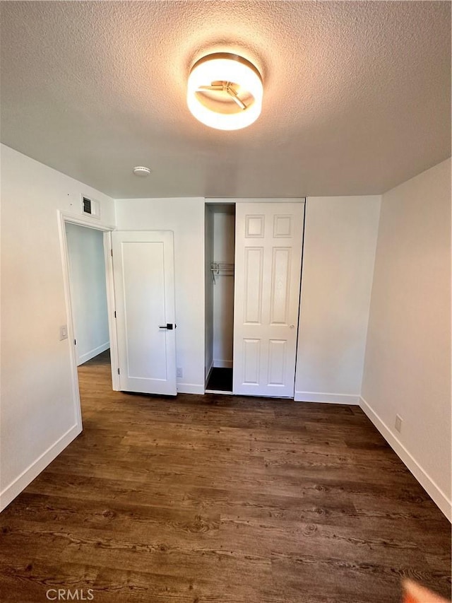 unfurnished bedroom featuring dark wood-style flooring, a closet, visible vents, a textured ceiling, and baseboards