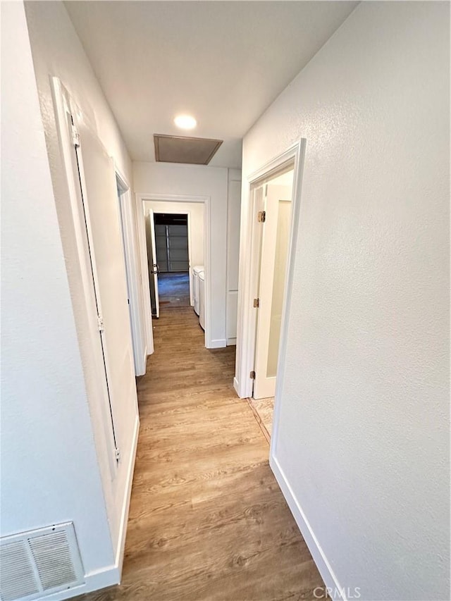 corridor with light wood-type flooring, independent washer and dryer, visible vents, and baseboards