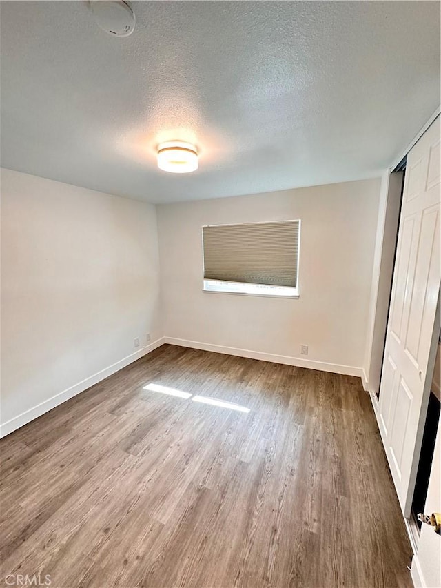 unfurnished bedroom with a textured ceiling, a closet, wood finished floors, and baseboards