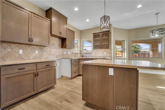 kitchen with light wood-type flooring, a kitchen island, decorative backsplash, and hanging light fixtures