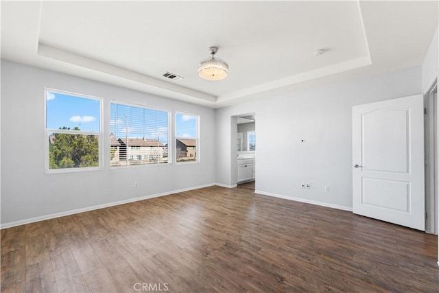 unfurnished room with dark wood-style floors, baseboards, visible vents, and a tray ceiling