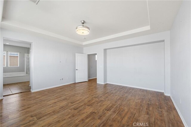 unfurnished bedroom with ensuite bathroom, a tray ceiling, wood finished floors, and baseboards