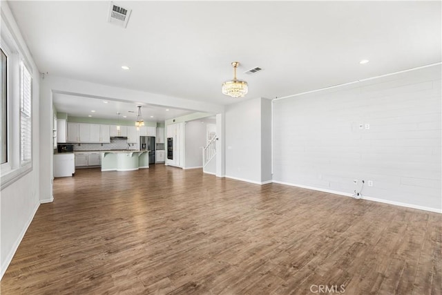 unfurnished living room featuring a notable chandelier, visible vents, and dark wood-style flooring