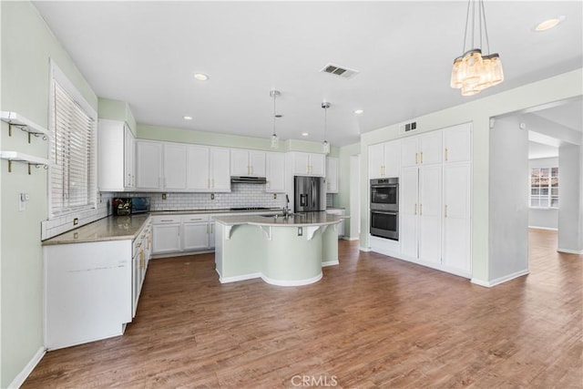 kitchen featuring tasteful backsplash, visible vents, a kitchen breakfast bar, stainless steel appliances, and under cabinet range hood