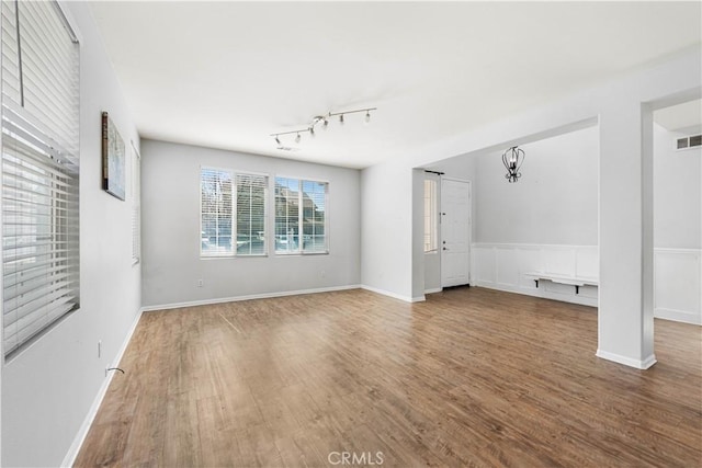 unfurnished living room featuring a chandelier, visible vents, baseboards, and wood finished floors